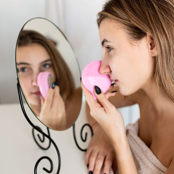 Nettoyeur facial électrique rose utilisé devant un miroir, soin de peau en profondeur.